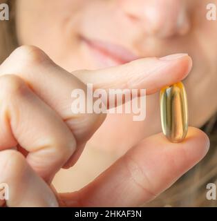 Femelle tenant en main la capsule en gel souple Omega 3. Gros plan, mise au point sélective. Banque D'Images