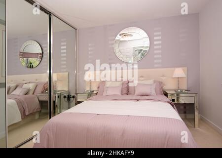 Chambre aux couleurs rose et blanc, avec mur, lampes de chevet, coussins, miroir sur le mur, tête de lit rembourrée, armoires à miroirs Banque D'Images