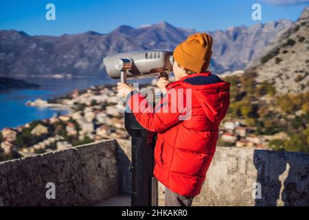 Jeune garçon touristique qui regarde à travers des jumelles et qui jouit d'une vue sur la baie de Kotor, au Monténégro.Echelle de la vieille ville de Kotor du sentier de randonnée de la forteresse de Kotor Banque D'Images