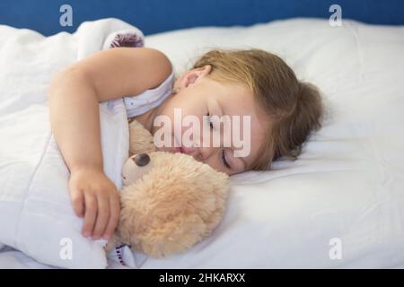 Enfant caucasien de trois ans dormant dans le lit avec un jouet ours pendant la journée Banque D'Images