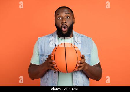 Photo de funky impressionné africain gars habillé jeans gilet de jeu de basket-ball isolé couleur orange fond Banque D'Images