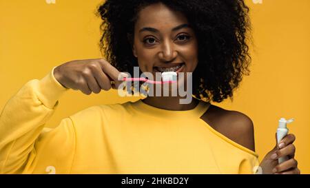 femme afro-américaine avec des bretelles souriantes et se brossant les dents isolées sur le jaune Banque D'Images