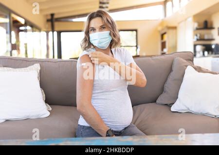 Femme enceinte caucasienne portant un masque facial montrant son épaule après avoir reçu le vaccin Banque D'Images