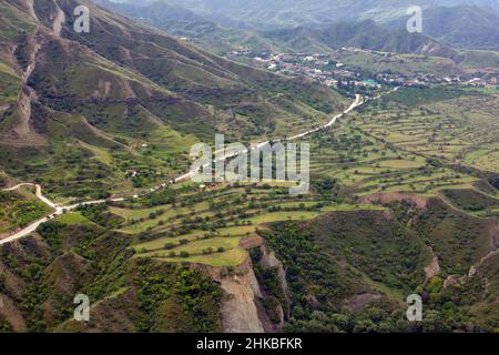 Route de gravier de terre à travers les montagnes rouges. Route dans un village isolé peuplé dans les montagnes. Village de haute montagne à Dagestan. Maisons sur un vert Banque D'Images