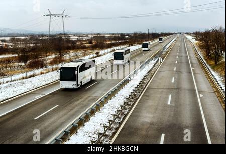 Série de bus White modernes voyageant sur une autoroute dans un paysage hivernal enneigé. Convoi de bus. Transport routier de passagers dans une ligne de bus Banque D'Images