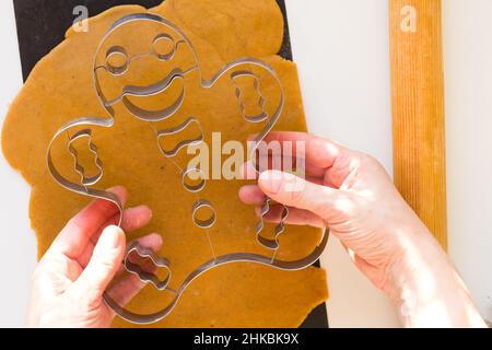 Femme mains tenant la forme métallique de pain d'épice homme avant du couper sur pâte brute feuille de téflon noir sur fond blanc Banque D'Images