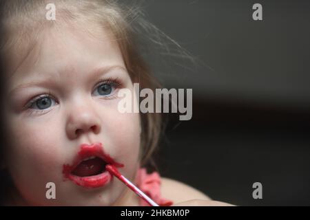 Bonne petite fille mettant rouge à lèvres sur les lèvres Banque D'Images