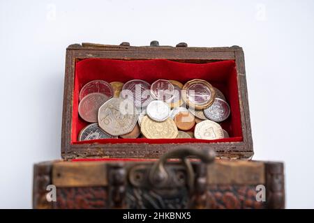 une petite vieille poitrine en bois avec des pièces sur fond blanc. épargne et inflation Banque D'Images
