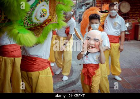 Une danseuse d'enfant est vue portant un masque de Bouddha entouré par d'autres membres de sa troupe de danse de lion le long de la rue.le nouvel an lunaire à Bangkok cette année est une affaire plus solennelle que les années précédentes.Le gouvernement avait techniquement annulé de grandes célébrations, mais dans le quartier chinois, une troupe de danseurs de lion ralentissait la circulation sur la route de Yaowrat.Dans une rue latérale de Wat Lokanukroh, la seule excitation pour la journée a été l'apparition d'un petit incendie causé par l'effondrement de grandes bougies rouges allumées l'une sur l'autre; les gardiens se sont précipités pour un extincteur.Beaucoup de thaïlandais d'origine chinoise ont continué à p Banque D'Images