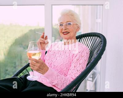 Ancienne femme élégante sénior sur la terrasse fumeur cigarette avec un verre de vin blanc.Mauvaise habitude, concept de dépendance Banque D'Images