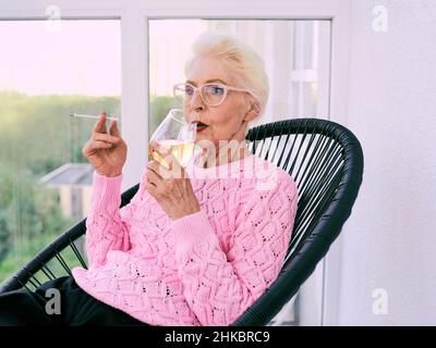 Ancienne femme élégante sénior sur la terrasse fumeur cigarette avec un verre de vin blanc.Mauvaise habitude, concept de dépendance Banque D'Images