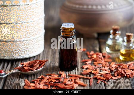 Une bouteille compte-gouttes d'huile essentielle d'aromathérapie avec des copeaux de bois de santal rouges et une lampe aromatique en arrière-plan Banque D'Images