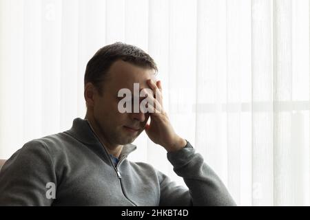 Homme fatigué avec les yeux fermés assis près d'une fenêtre, décontracté photo de studio Banque D'Images