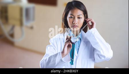 Jeune femme asiatique médecin examinant avec le stéthoscope pendant qu'elle est debout à l'hôpital Banque D'Images