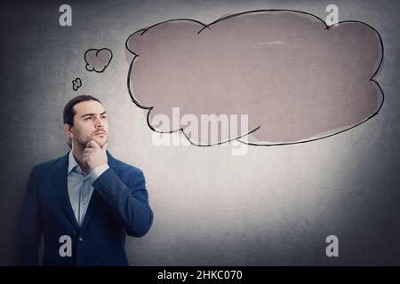 Homme d'affaires contemplant avec une main sous le menton, regardant loin pensif isolé sur le mur gris avec une bulle au-dessus de la tête.Activité réfléchie par Banque D'Images