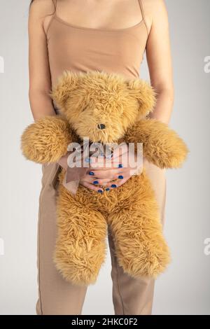 Femme et enfant, concept de mode.Femme fine et belle avec un pantalon beige et un t-shirt sans manches tenant l'ours brun peluche jouet dans ses mains. Banque D'Images