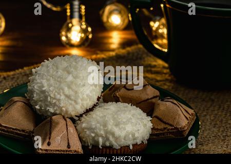 Gros plan de gâteaux soufflés avec flocons de noix de coco et biscuits croustillants sur une soucoupe avec une tasse de café ou de thé.Photo dans une touche sombre, lumière tamisée et chaude Banque D'Images