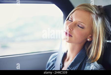 Conduite dans le luxe.Photo d'une jeune femme attirante endormie dans le siège arrière d'une voiture pendant un voyage en voiture. Banque D'Images
