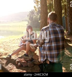 Profiter d'un voyage de camping frais.Prise de vue d'une jeune femme jouant de la guitare pour son petit ami à leur campement. Banque D'Images