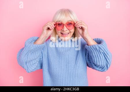 Portrait d'une femme joyeuse et attrayante aux cheveux gris touchant des lunettes isolées sur fond rose pastel Banque D'Images