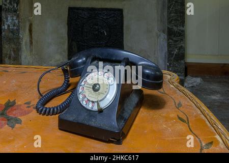 Très vieux téléphone noir avec des pieds de téléphone sur une table dans une ancienne maison abandonnée Banque D'Images