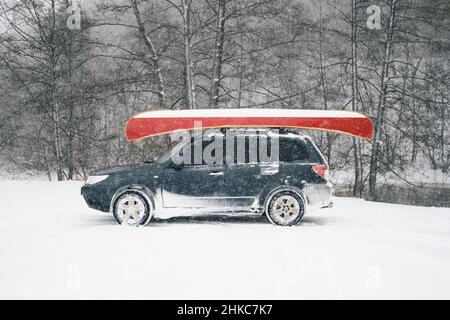 Une voiture avec un canot canadien sur le toit au bord de la rivière en hiver. Banque D'Images