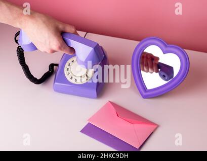 Femme tenant le combiné téléphonique rétro. Téléphone de style vintage sur table avec miroir en forme de coeur et enveloppes. Concept Saint Valentin et amour. Photo de haute qualité Banque D'Images