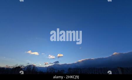 Les nuages sombres en time lapse cachent le soleil du soir au coucher du soleil, et ciel bleu clair.Les branches des arbres oscillent dans le vent en hiver Banque D'Images