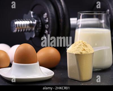 œufs, cuillère de poudre de protéine de lactosérum, verre de lait et haltères sur fond noir, concept de nutrition sportive Banque D'Images