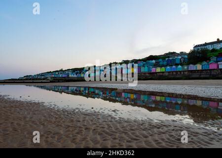 Des cabanes de plage colorées bordent la promenade de Walton-on-the-Naze, sur la côte nord de l'Essex, au Royaume-Uni.Réflexions créées dans les bassins laissés à marée basse. Banque D'Images