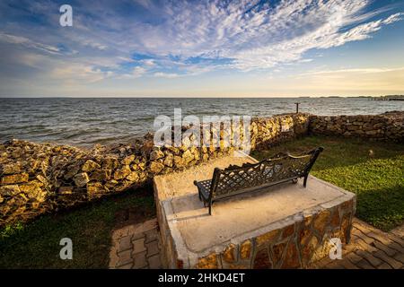 Vue sur un banc de parc vide en fer forgé surplombant les eaux agitées du lac Victoria à Entebbe, en Ouganda Banque D'Images