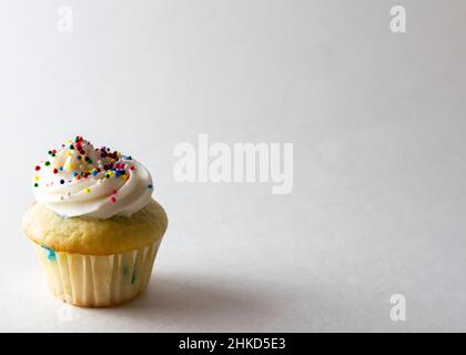 Vue rapprochée d'un mini-cupcake décoré de mini-boules de bonbons saupoudrés de couleur ressort.Arrière-plan blanc avec espace de copie. Banque D'Images
