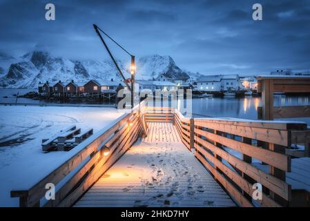 Jetée en bois enneigé sur la côte de la mer avec lumières, rorbu, montagnes Banque D'Images