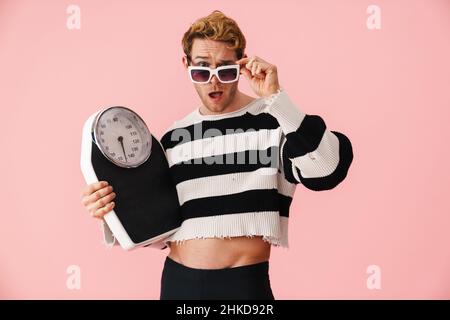 Gingembre jeune homme choqué portant des lunettes de soleil posant avec des balances isolées sur le mur rose Banque D'Images