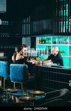 Le barman verse des cocktails à un jeune couple dans un restaurant Banque D'Images