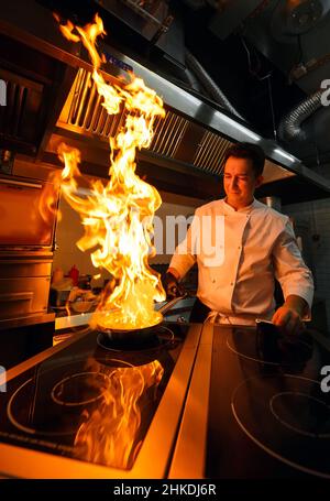 Gros plan sur les mains du chef cuisant des aliments au feu.Le chef brûle des aliments dans une cuisine professionnelle Banque D'Images