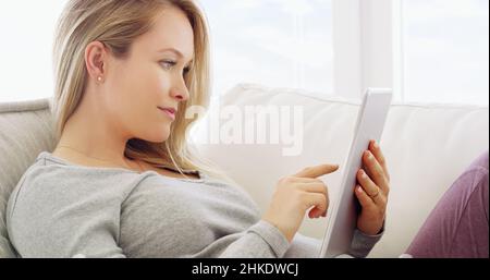 La connectivité à portée de main.Prise de vue d'une femme enceinte utilisant un comprimé à la maison. Banque D'Images