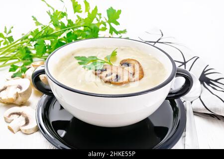 Soupe de purée de champagnes, pommes de terre, oignons et crème dans un bol, serviette, persil et cuillère sur fond de bois blanc Banque D'Images