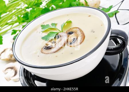 Soupe de purée de champagnes, pommes de terre, oignons et crème dans un bol, une serviette, persil et une cuillère sur fond de bois clair Banque D'Images