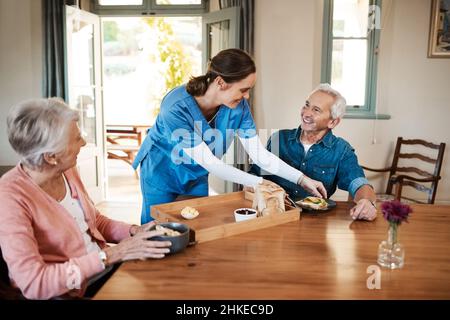 C'est encore mieux qu'un restaurant.Prise de vue d'une jeune infirmière qui s'est mise à vérifier sur un couple senior pendant le petit-déjeuner dans une maison de soins infirmiers. Banque D'Images