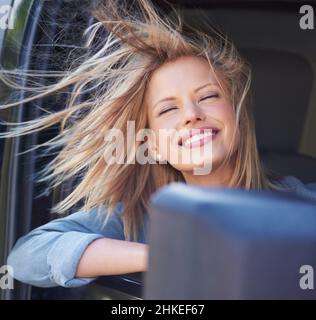 Sentez le vent dans vos cheveuxUne jeune femme ressent la brise dans ses cheveux à travers une fenêtre de voiture ouverte. Banque D'Images