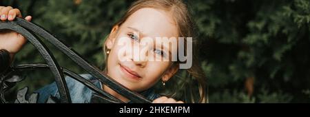 portrait sérieux sérieux et sincère jeune fille de huit ans visage peeking hors de formes métalliques abstraites dans la nature. âge prépubertaire des enfants et de leurs Banque D'Images