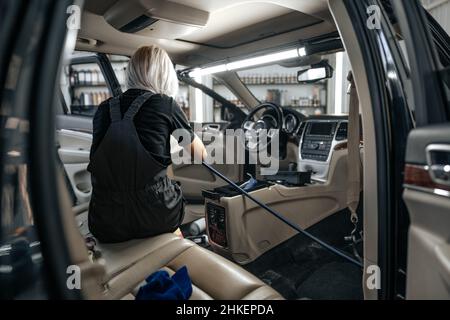 Femme travailleuse aspirant poussière intérieur de la voiture dans le lave-auto. Banque D'Images