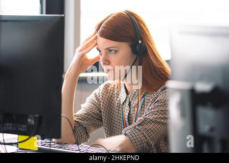 Belle jeune caucasienne rouge cheveux fille avec les mains sur la tête dressing décontracté avec mal de tête ou migraine travaillant dans le bureau ou la classe au bureau Banque D'Images