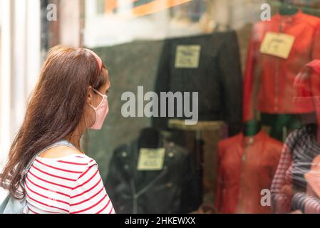 Femme anonyme en masque regardant la vitrine Banque D'Images