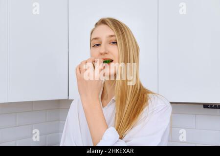 Une femme délicate mord un morceau de concombre tout en faisant de la salade de légumes Banque D'Images