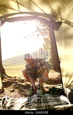 Dans les bois.Photo d'un jeune homme faisant du café sur un poêle de camp pendant le camping. Banque D'Images