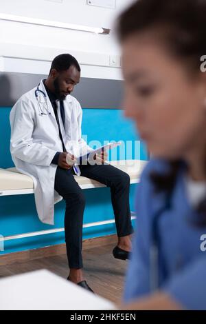 Médecin généraliste avec une blouse regardant les documents de contrôle, attendant le patient à un rendez-vous d'examen au bureau médical.Articles de lecture spécialisés pour traiter les maladies et les maladies Banque D'Images