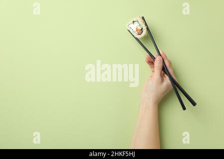 La main femelle contient des sushis avec des baguettes sur fond vert Banque D'Images
