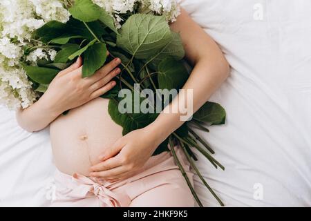 Coupe courte belle jeune femme enceinte 20s couché sur un confortable lit blanc avec fleur de printemps fraîche, aime le matin et la grossesse merveilleux.Copier Banque D'Images